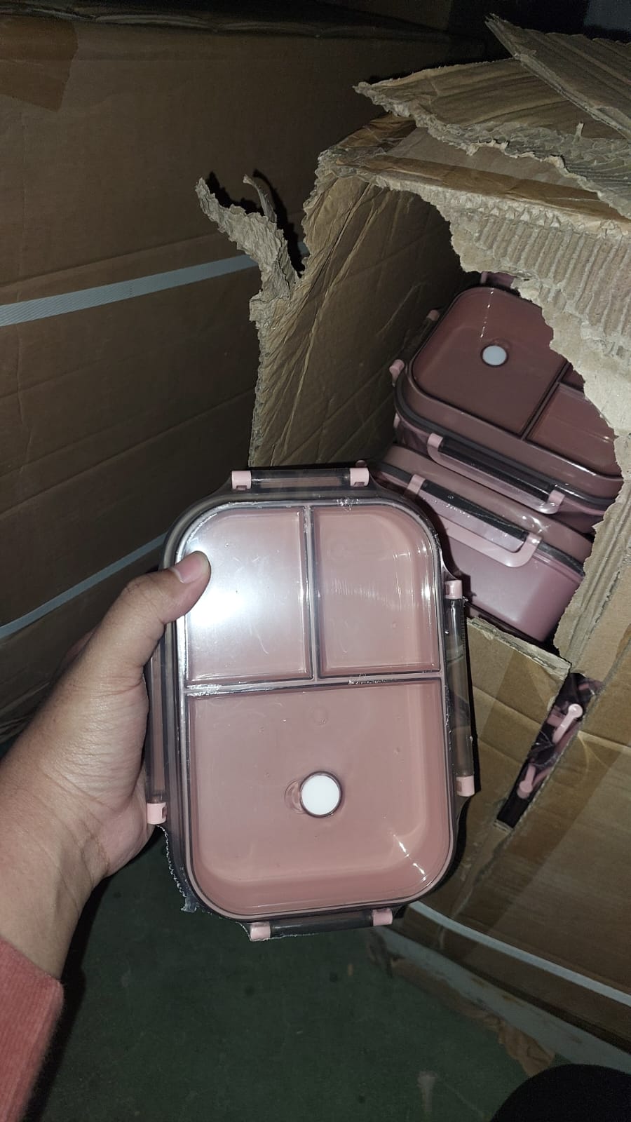 Compact makeup case held by a hand with cardboard boxes in the background
