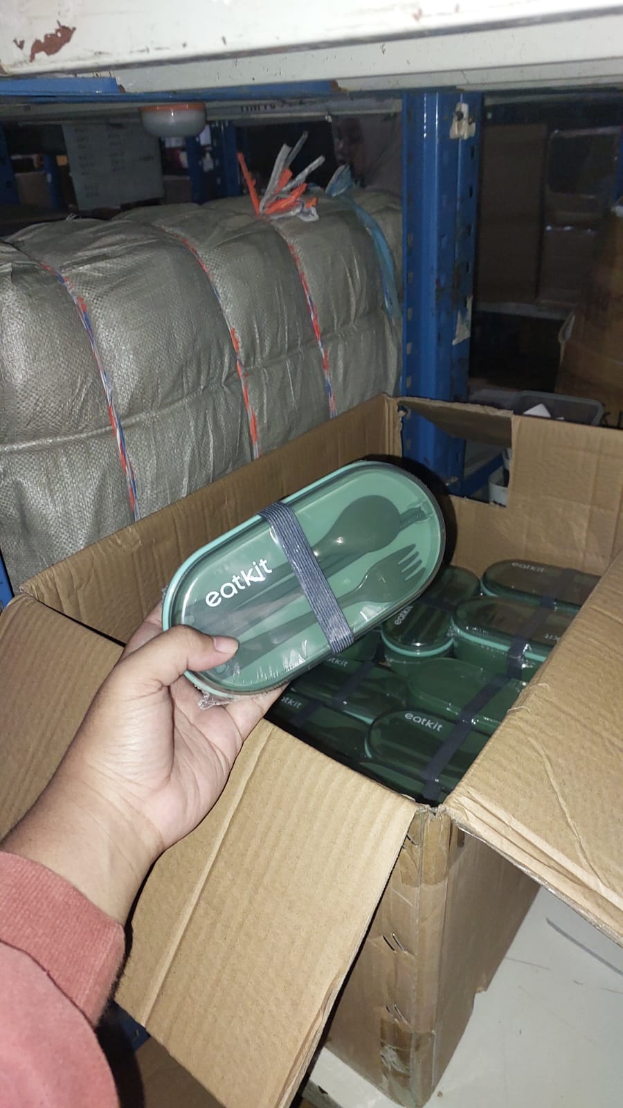 Person holding a green container with 'Eatkit' branding inside a cardboard box.