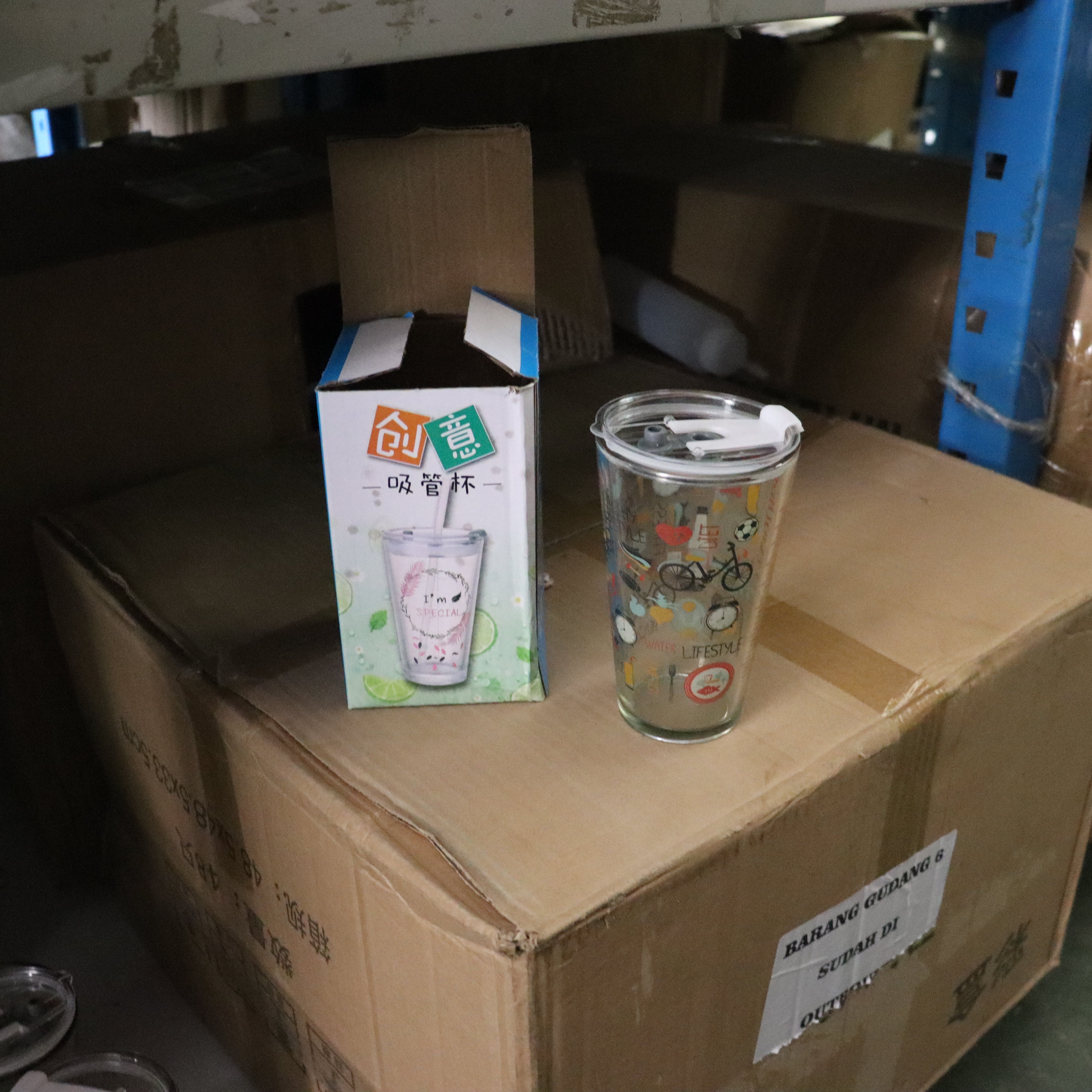 Glass tumbler with colorful design on a cardboard box with packaging box in the background.