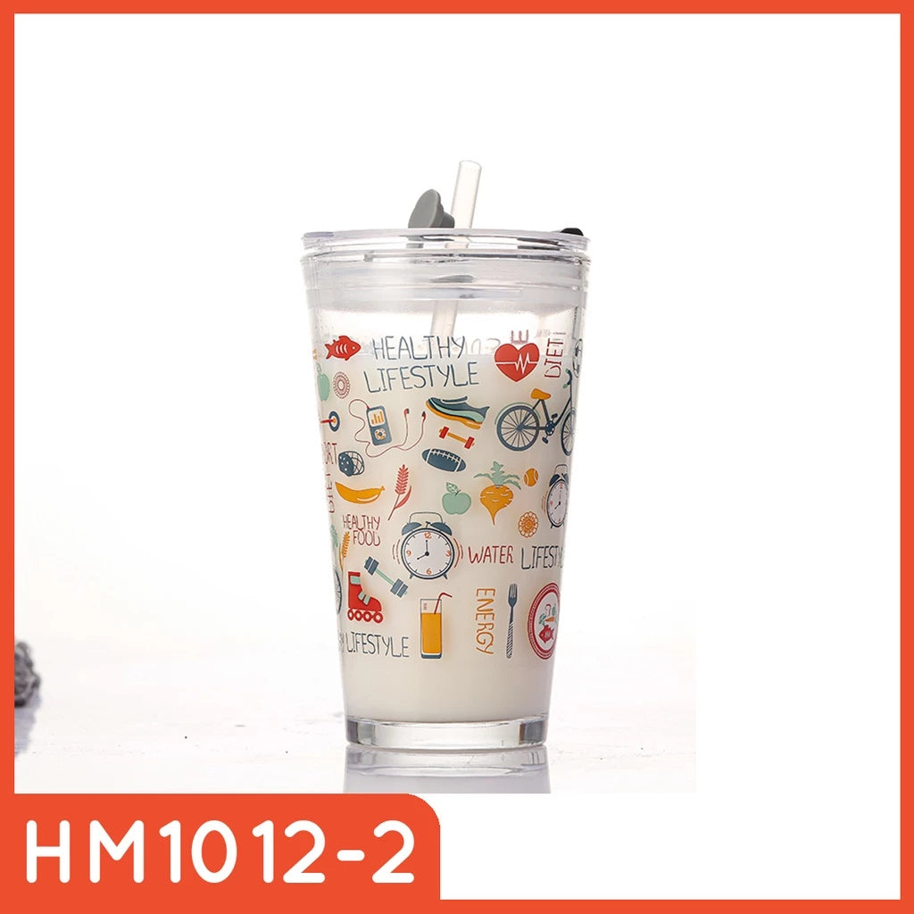 Gelas tumbler kaca transparan berisi cairan putih, dihiasi ilustrasi warna-warni bertema hidup sehat seperti sepeda, barbel, makanan sehat, dan jam. Terdapat tulisan "HEALTHY LIFESTYLE", "DIET", "ENERGY", dan "WATER LIFESTYLE", serta dilengkapi sedotan dan tutup hitam.