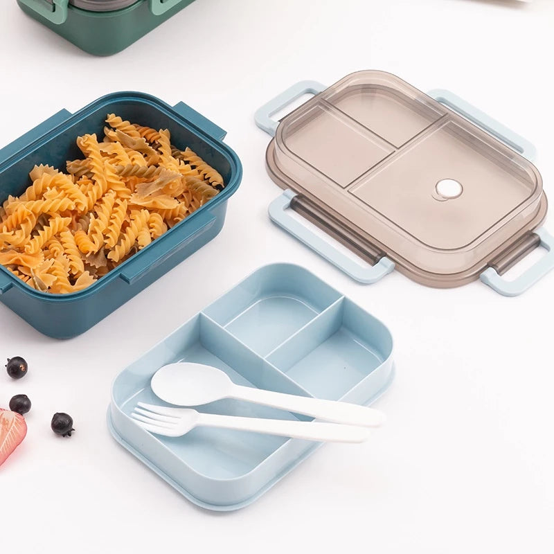 Komponen kotak makan siang dua tingkat yang dibongkar dan tersebar: wadah bawah teal berisi pasta fusilli, baki tengah biru muda dengan tiga sekat dan sendok garpu putih, serta tutup transparan dengan klip pengunci biru muda. Kotak makan siang hijau tua lainnya terlihat sebagian di sudut atas.