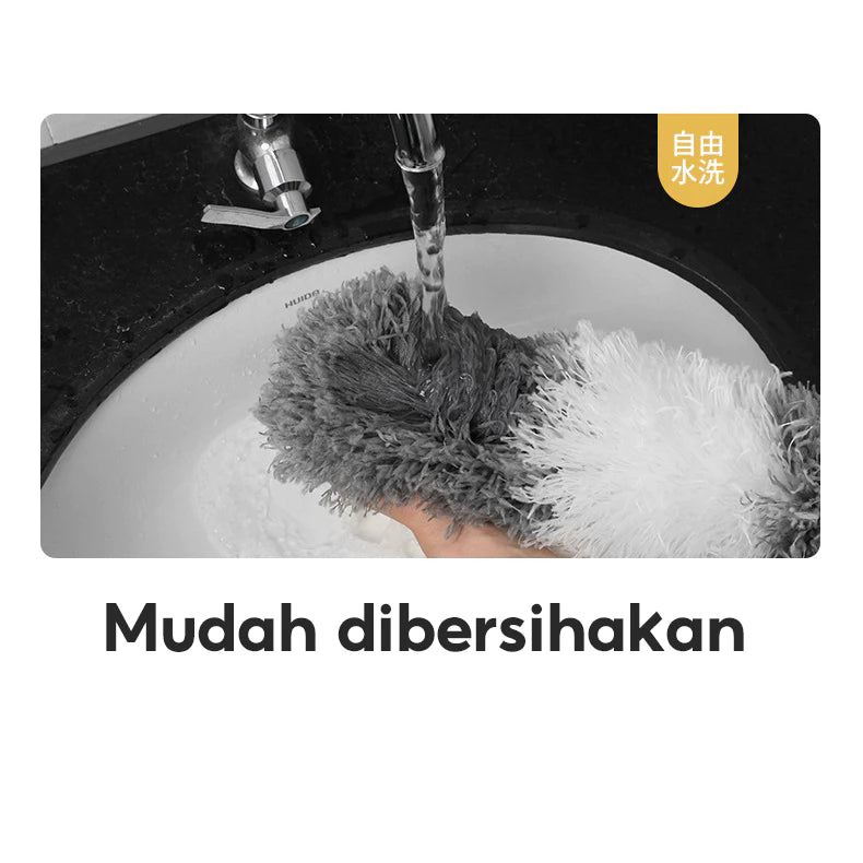 Gambar ini menampilkan tangan yang memegang kepala kemoceng microfiber berwarna abu-abu dan putih di bawah aliran air keran. Kepala kemoceng sedang dibilas di dalam wastafel putih, menunjukkan kemudahan dalam membersihkannya