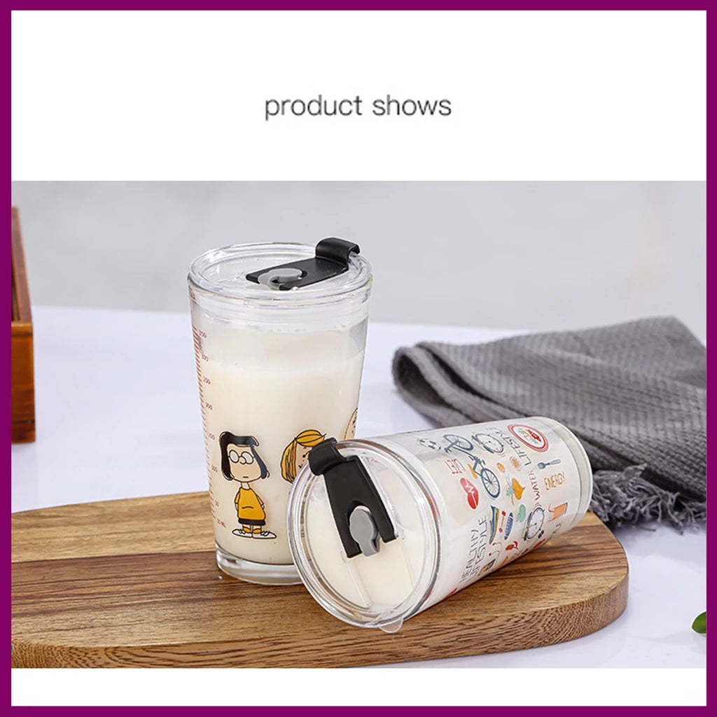 Dua gelas tumbler kaca berisi cairan putih, diletakkan di atas talenan kayu. Satu gelas berdiri tegak dengan desain karakter Snoopy dan Charlie Brown, dan gelas lainnya tergeletak miring dengan ilustrasi tema hidup sehat. Keduanya memiliki tutup hitam dengan mekanisme minum.