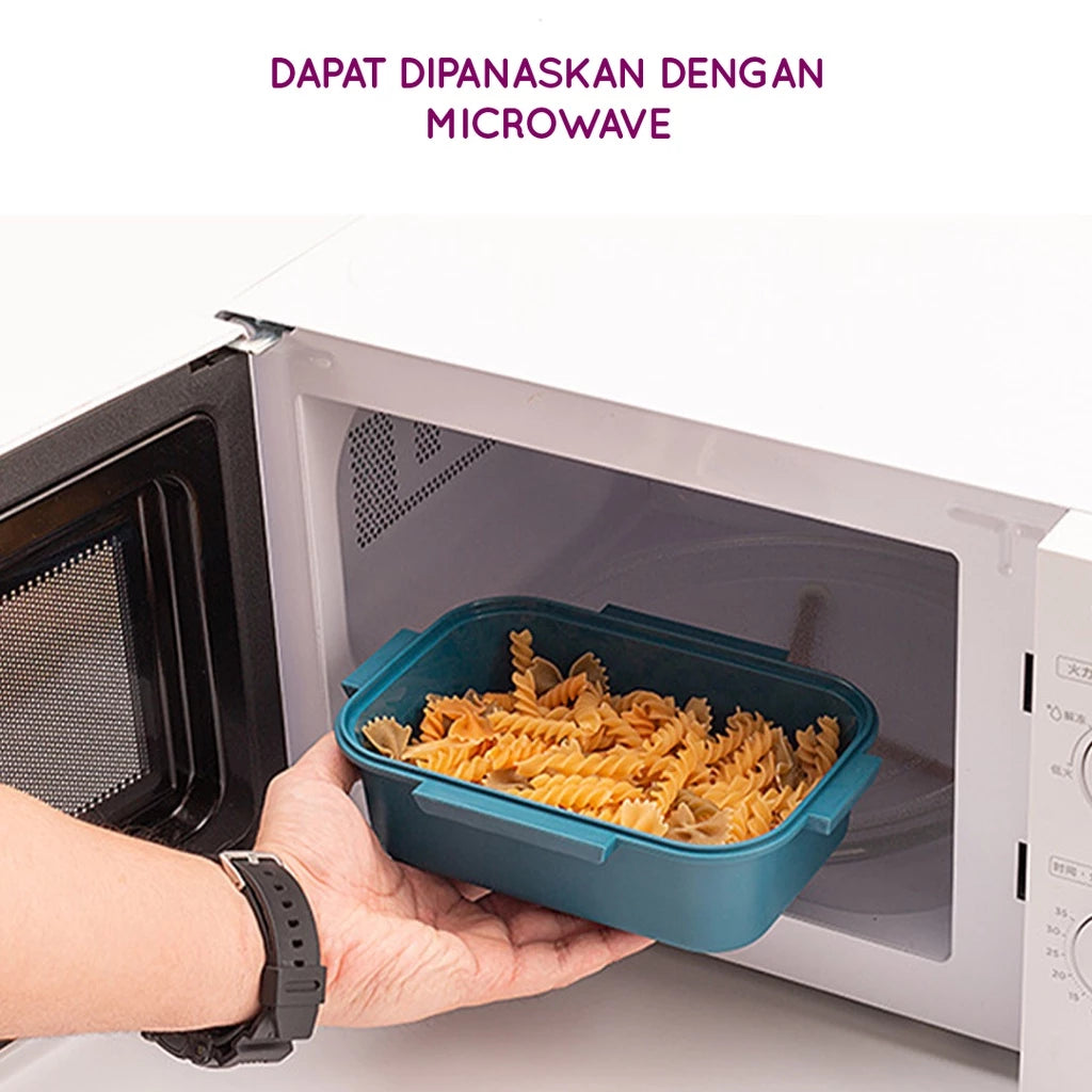 Sebuah tangan memasukkan wadah bawah kotak makan siang berwarna teal yang penuh dengan pasta fusilli ke dalam microwave putih, menunjukkan bahwa produk aman untuk digunakan dalam microwave.