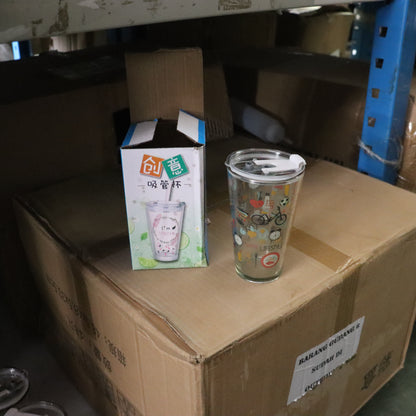 Glass tumbler with colorful design on a cardboard box with packaging box in the background.