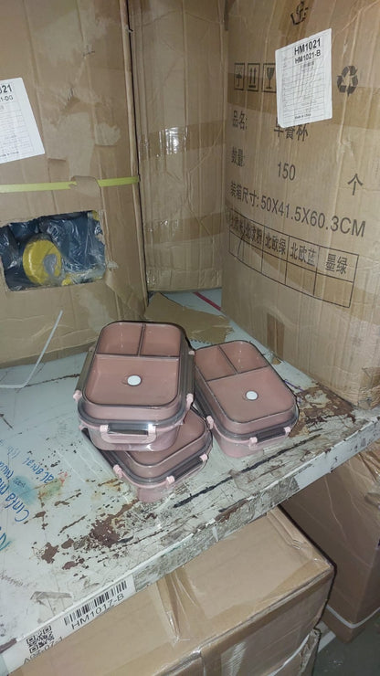 Stack of pink food containers on a cluttered surface with cardboard boxes and labels in the background.