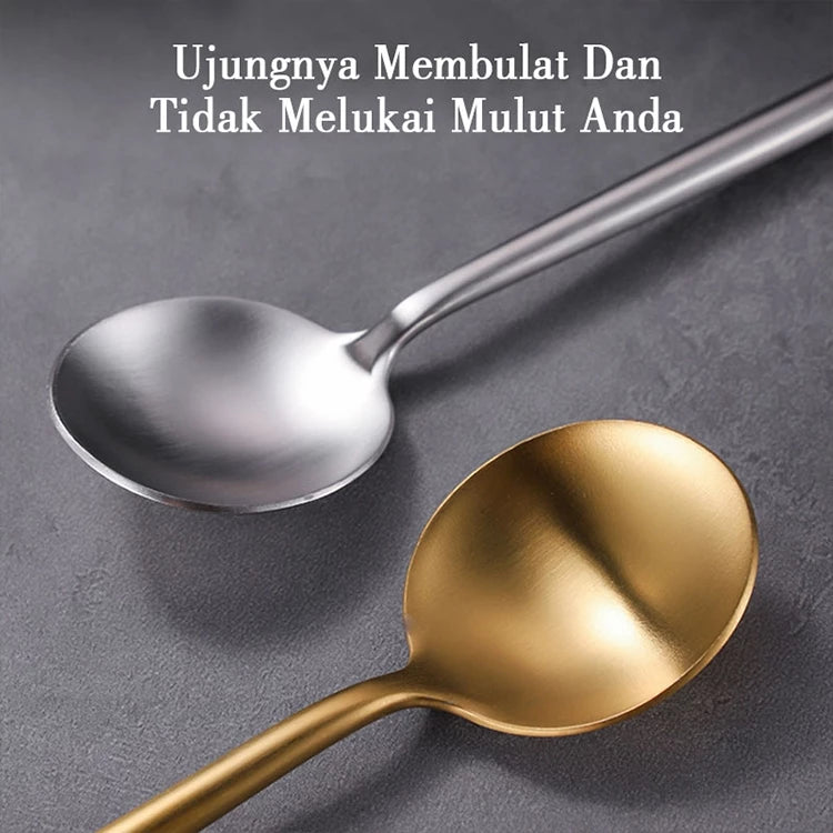 
Sebuah sendok perak matte dan sendok emas matte diletakkan secara diagonal di permukaan gelap, dengan teks "Ujungnya Membulat Dan Tidak Melukai Mulut Anda" di bagian atas.