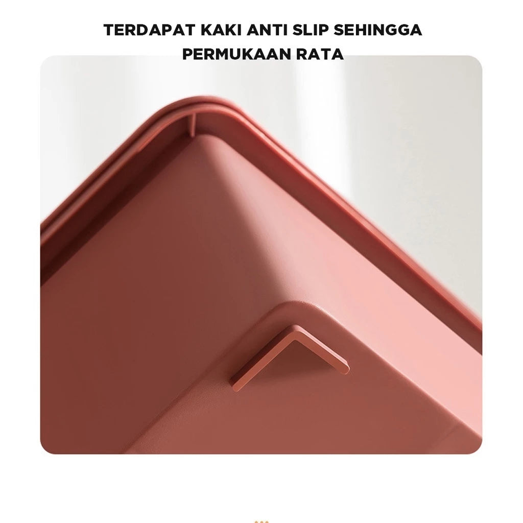 Tampilan dekat sudut bawah kotak penyimpanan berwarna merah muda salmon, menyoroti fitur kaki anti-selip kecil yang menonjol untuk menjaga permukaan tetap rata dan stabil. Teks di atas gambar menyatakan 'TERDAPAT KAKI ANTI SLIP SEHINGGA PERMUKAAN RATA'."