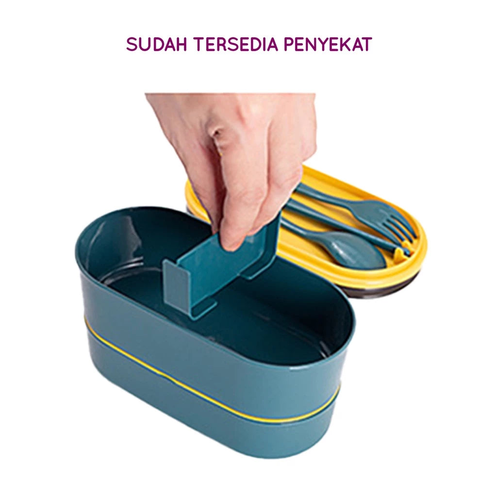 Kotak makan siang dua tingkat warna teal dan kuning dengan sekat yang dapat dilepas, dipegang oleh tangan, dan set sendok garpu yang serasi di sebelahnya.

