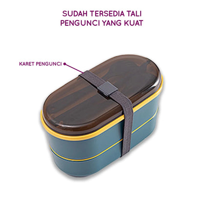 Kotak makan siang dua tingkat berwarna teal dengan aksen kuning di bagian bawah, tutup transparan, dan sendok garpu yang diletakkan di dalamnya, diikat dengan tali pengunci elastis berwarna abu-abu gelap.

